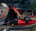Close-up of a car battery with attached jumper cables in an engine bay.